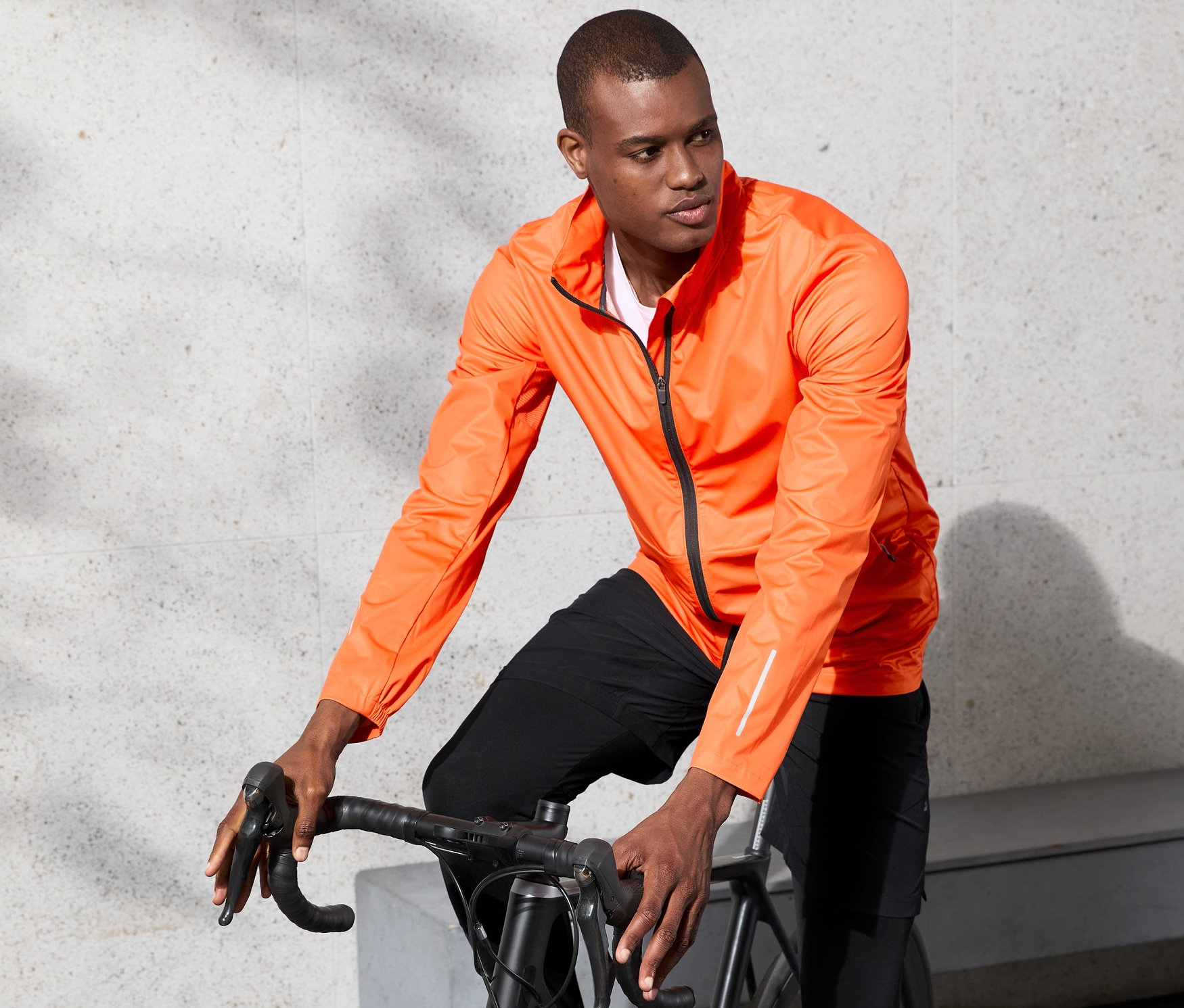 Férfi kerékpározik narancssárga, szélálló futódzsekiben.