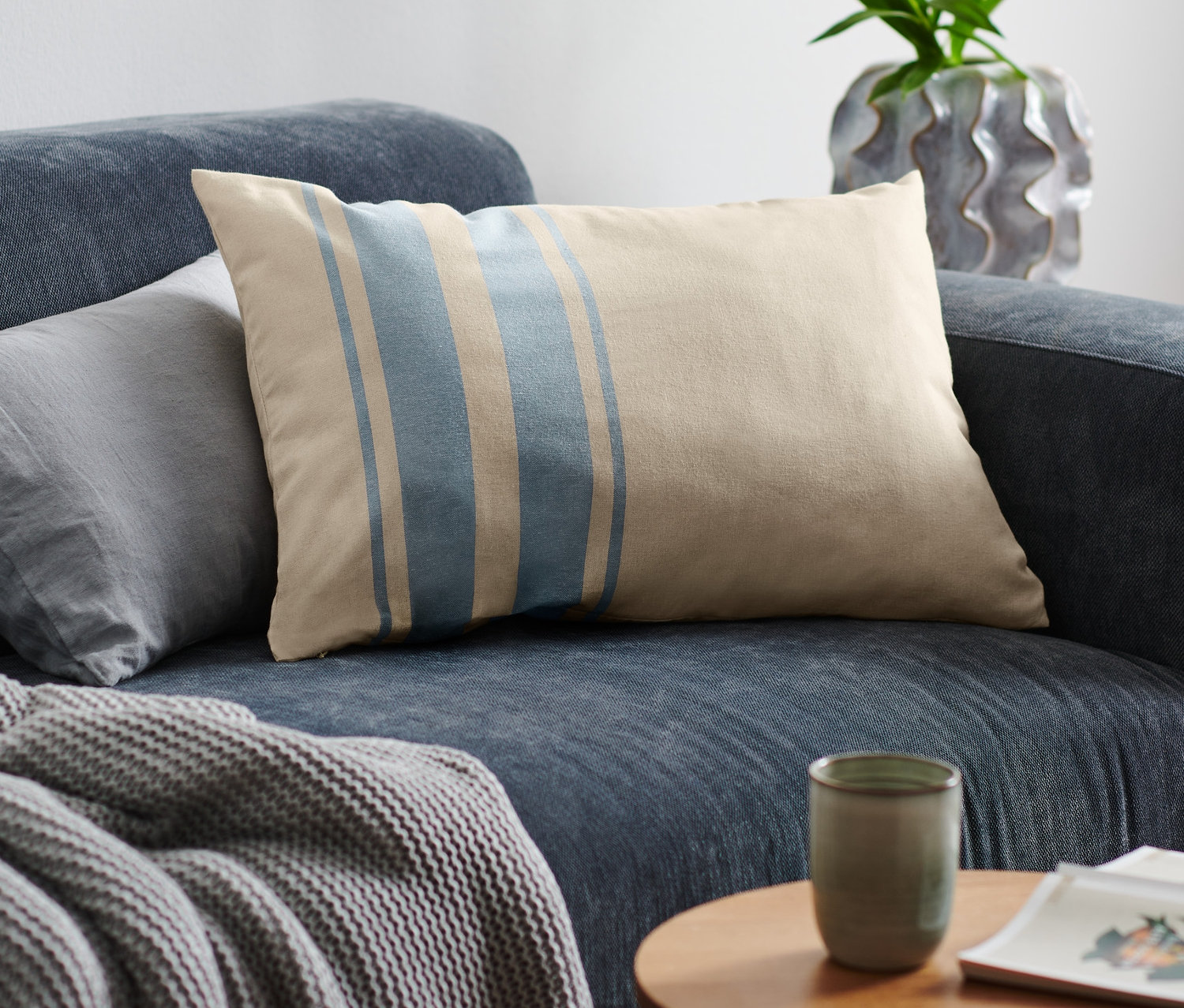 A kék kanapén egy bézs színű, kék csíkos díszpárnahuzat látható.