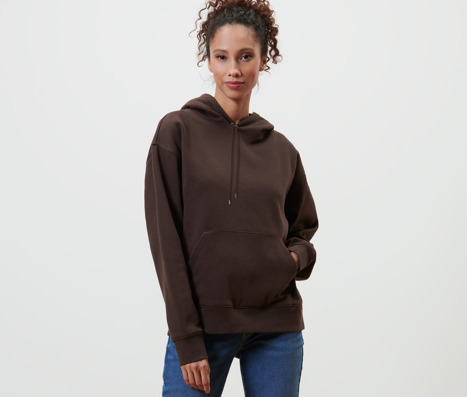Egy nő pózol egy sötétbarna kapucnis pulóverben.
