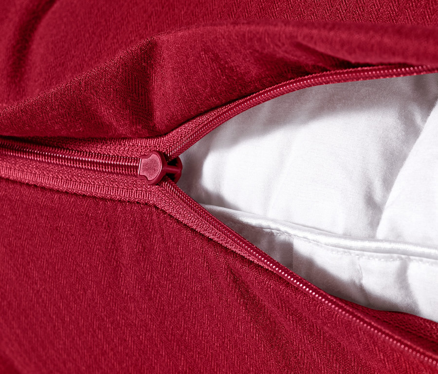 Egy piros, 80 x 40 cm-es mikroflanel párnahuzat részlete, nyitott cipzárral, ami láthatóvá teszi a fehér töltetet.