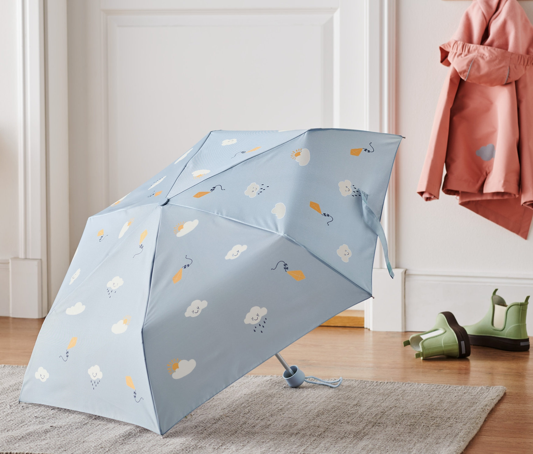 Egy világoskék, felhős mintázatú táskaesernyő fekszik egy szürke szőnyegen.