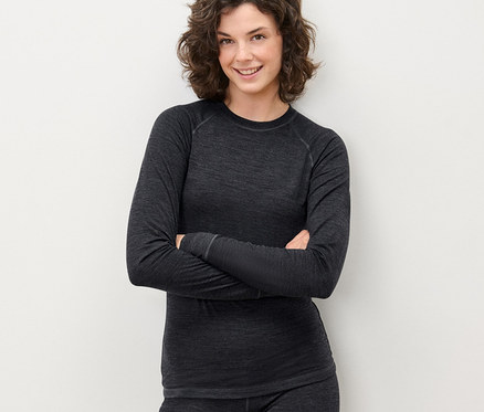 Egy nő keresztbe tett karokkal pózol egy szürke, RWS-tanúsítvánnyal rendelkező gyapjú funkcionális pólóban és nadrágban.