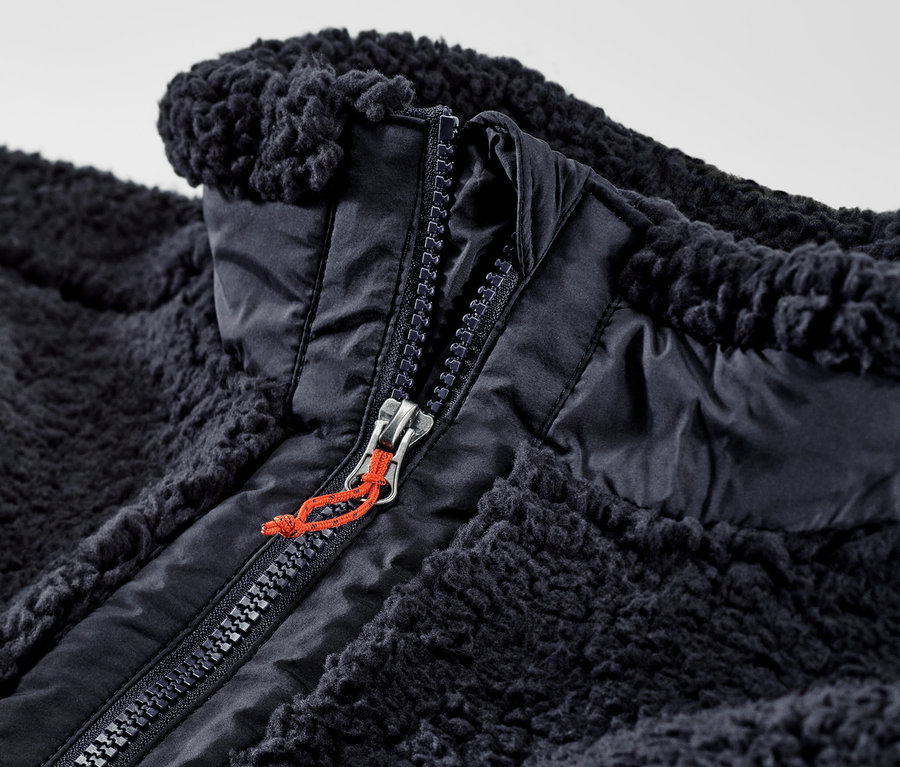 Közelkép egy nyitott, cipzáras, sötétkék férfi plüssmellényről.