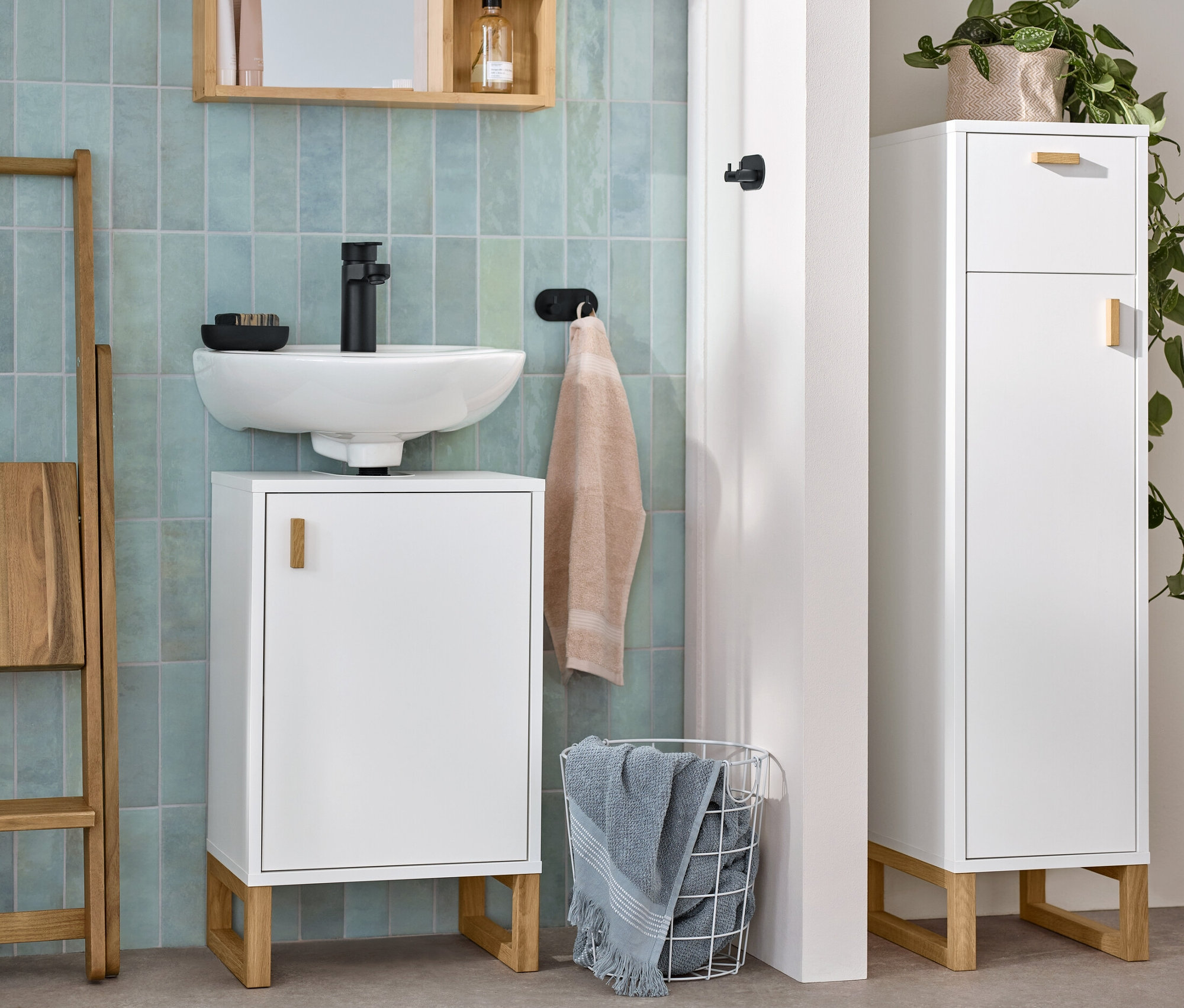 Egy fürdőszoba látható egy mosdó alatti szekrénnyel, egy keskeny fürdőszobai szekrénnyel és egy tükörrel.