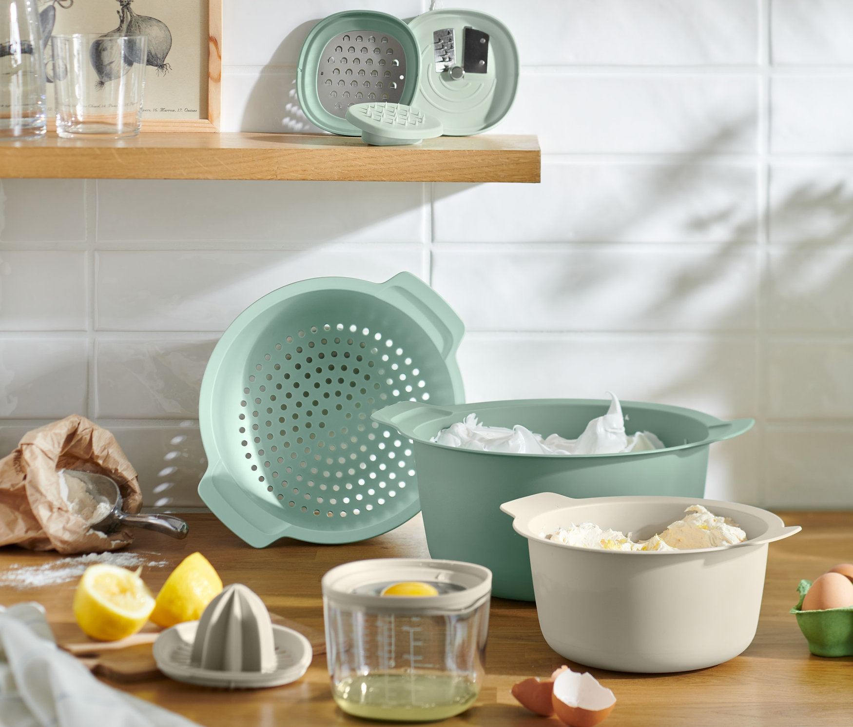 Konyhai eszközök és hozzávalók egy fafelületen, beleértve egy tálat, szűrőt, citrusfacsarót, tojásokat és lisztet.