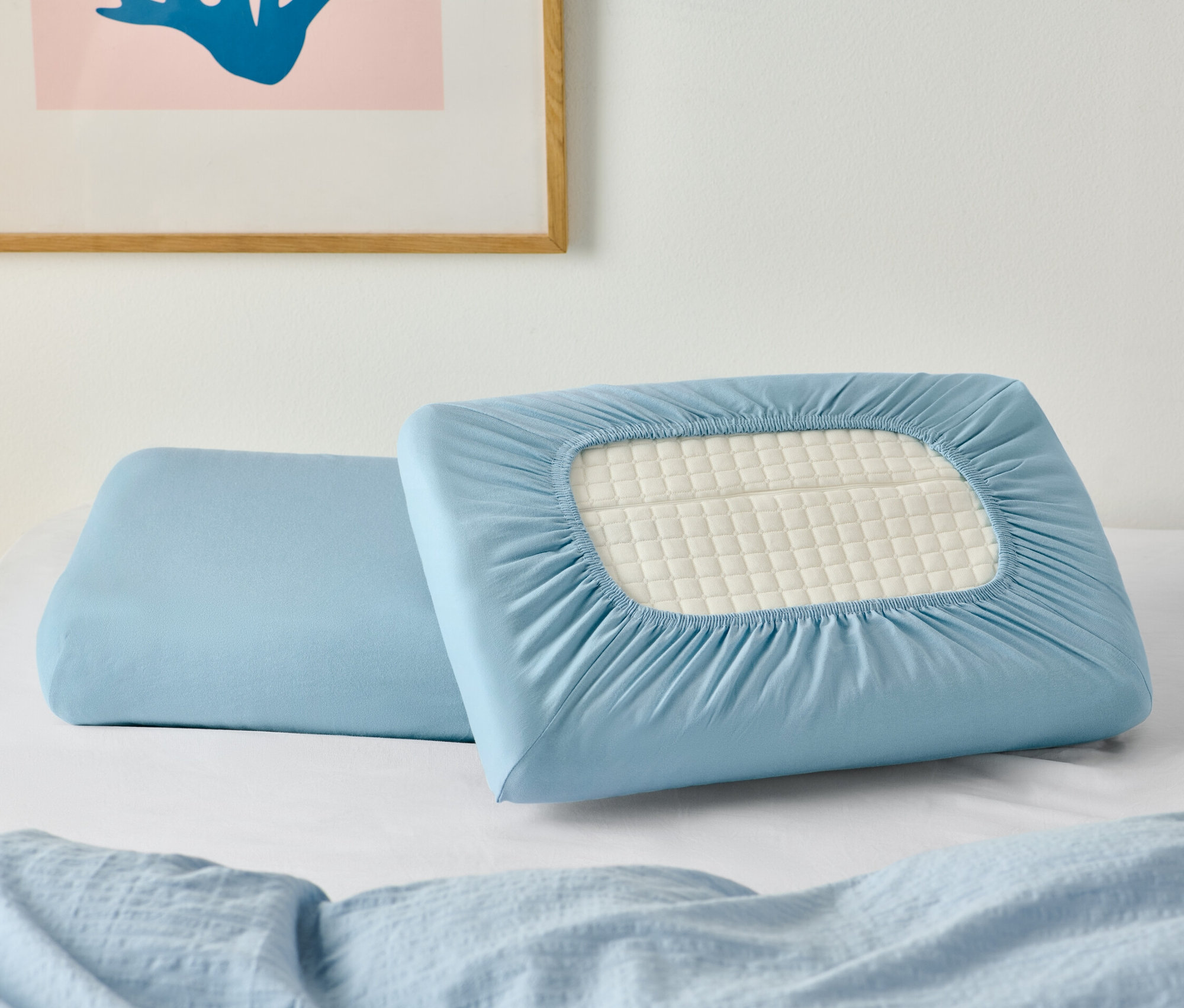 Két gumis jersey párnahuzat egy fehér lepedőn, egy kép alatt.