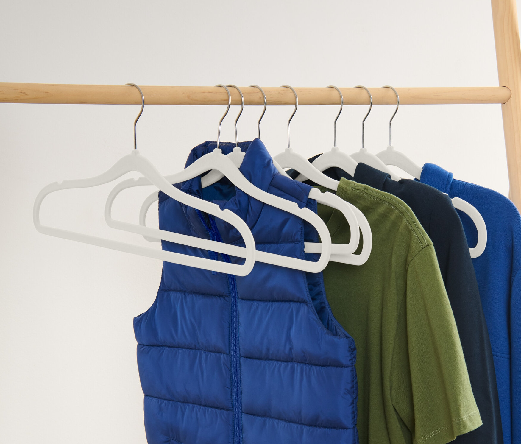 Egy kék mellény és egy zöld, sötétkék és kék póló lóg 8 különösen keskeny vállfán.