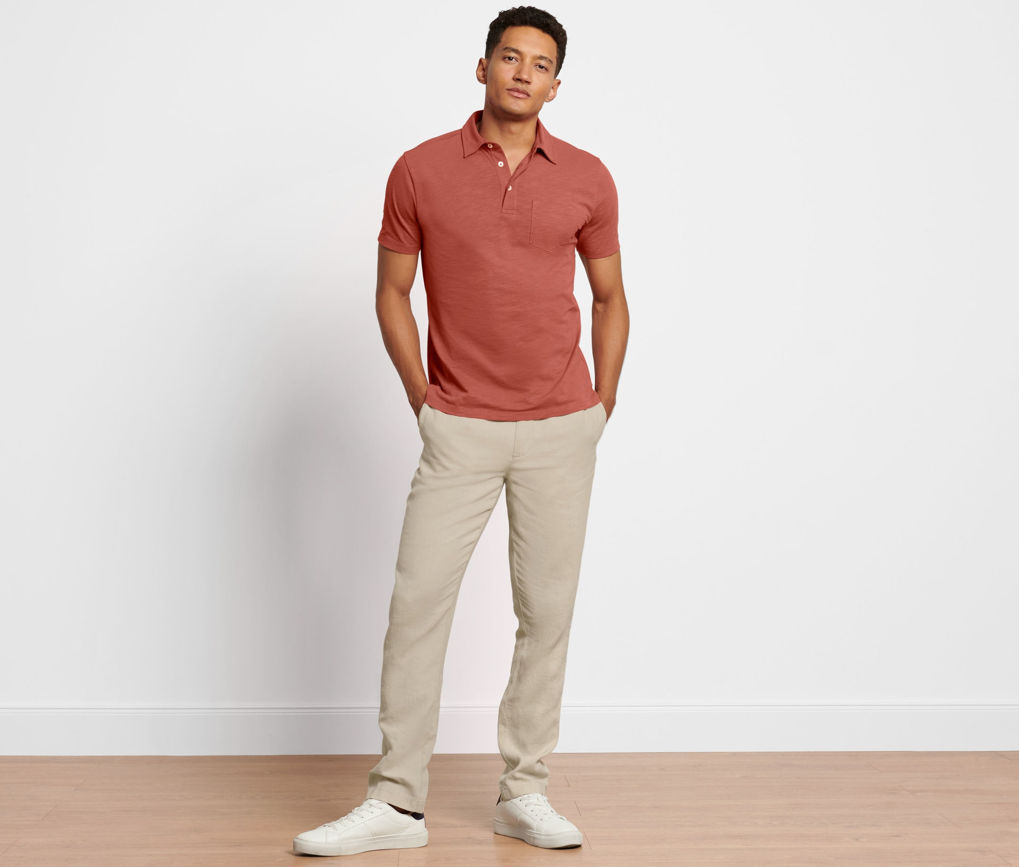 Egy férfi lenvászon chino nadrágban és vörösbarna pólóban pózol.