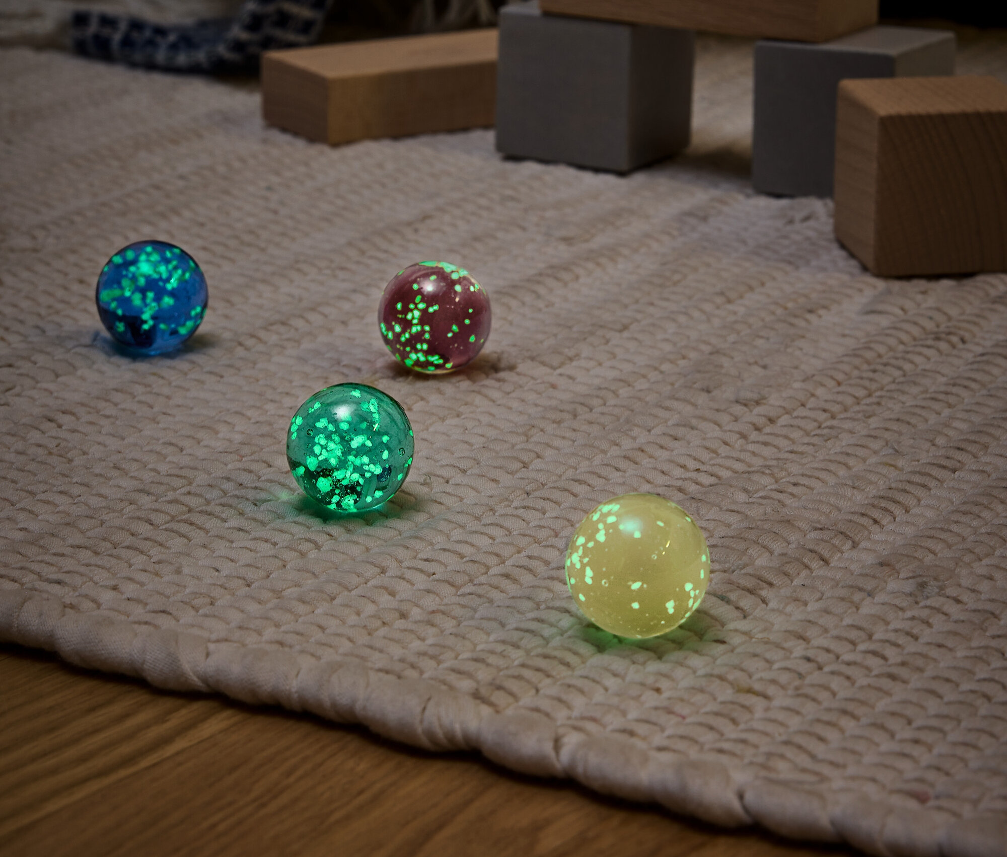 Négy különböző színű (kék, piros, zöld és sárga) világító gömb egy bézs szőnyegen, háttérben fa játékokkal.
