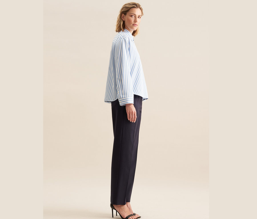 Nő pózol kék Seidensticker túlméretes női ingblúzban és sötétkék nadrágban.