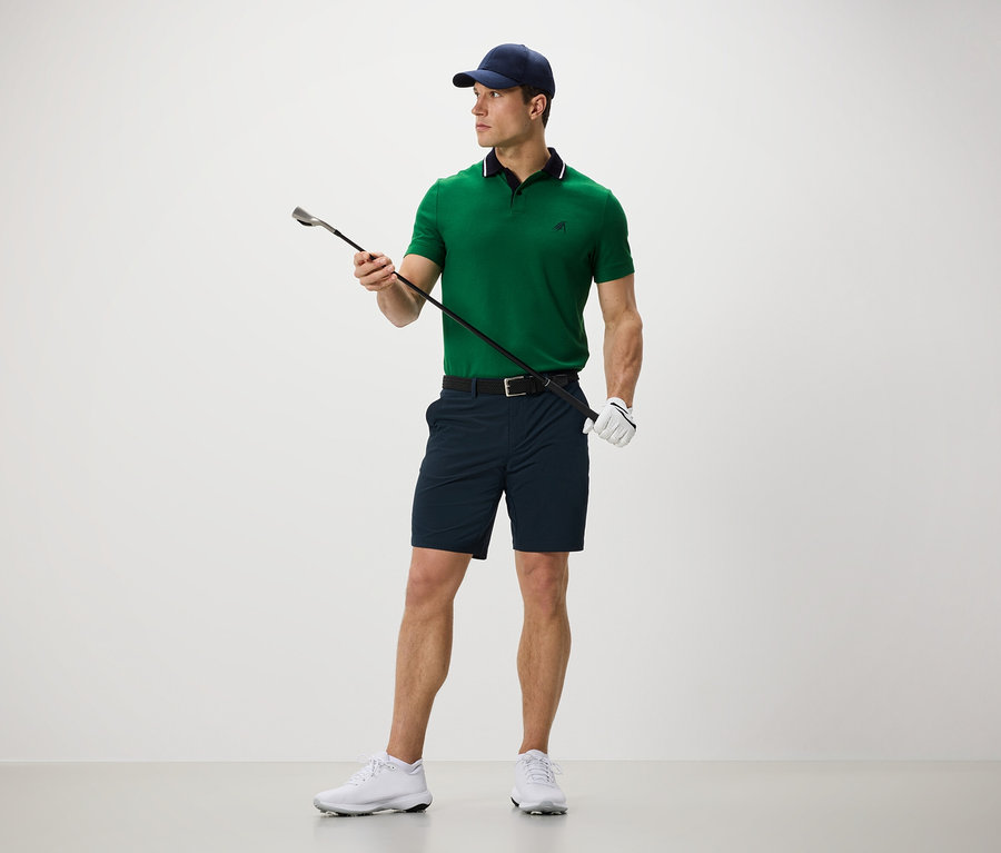 Férfi golfütőt tart és fekete funkcionális rövidnadrágot visel.