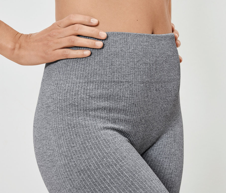 Nő pózol szürke, bordázott leggingsben.