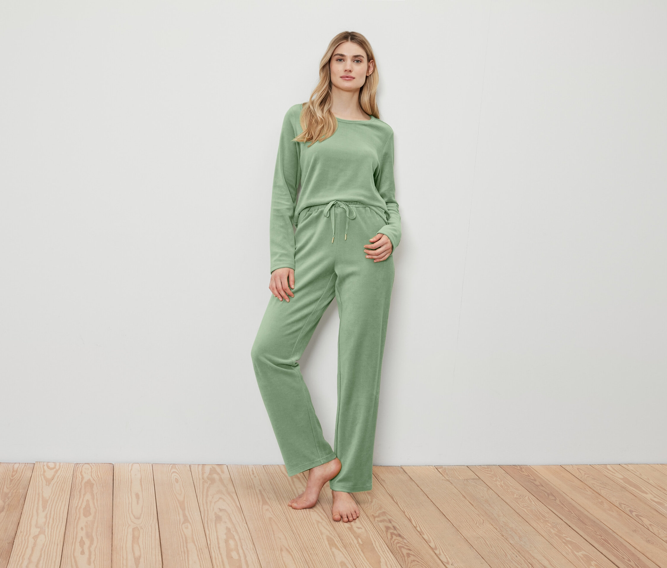 Nő pózol zöld pulóverben és nadrágban.