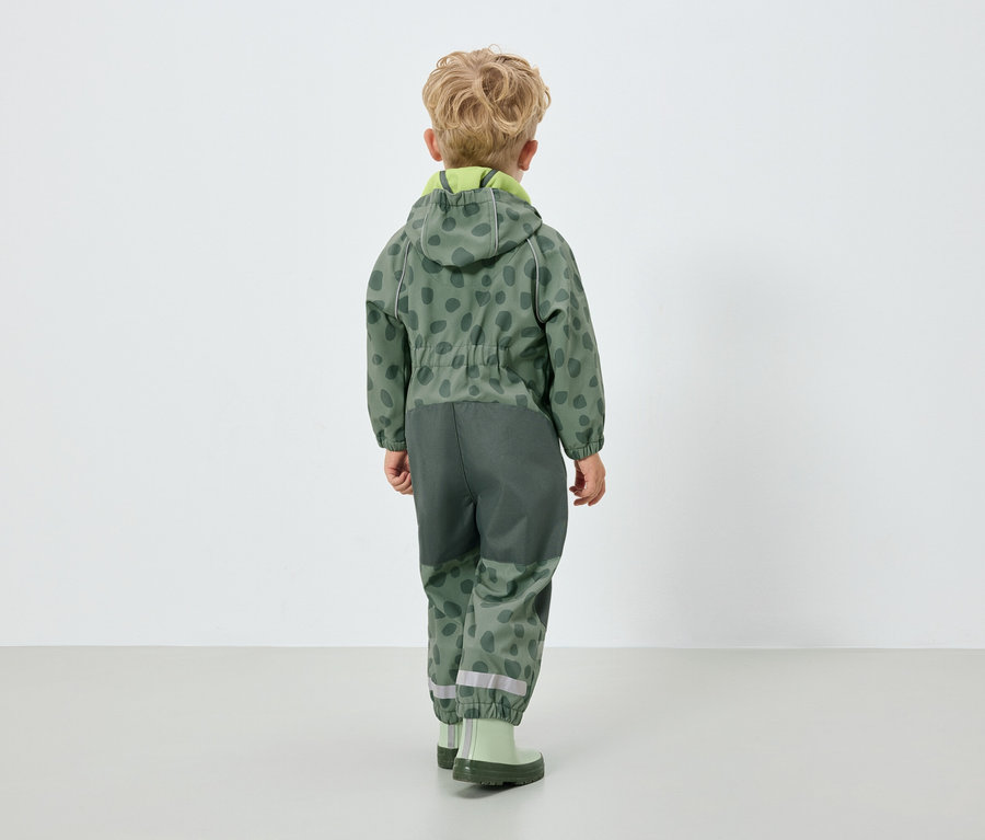 Fiú zöld, kapucnis overallban, háttal a kamerának.