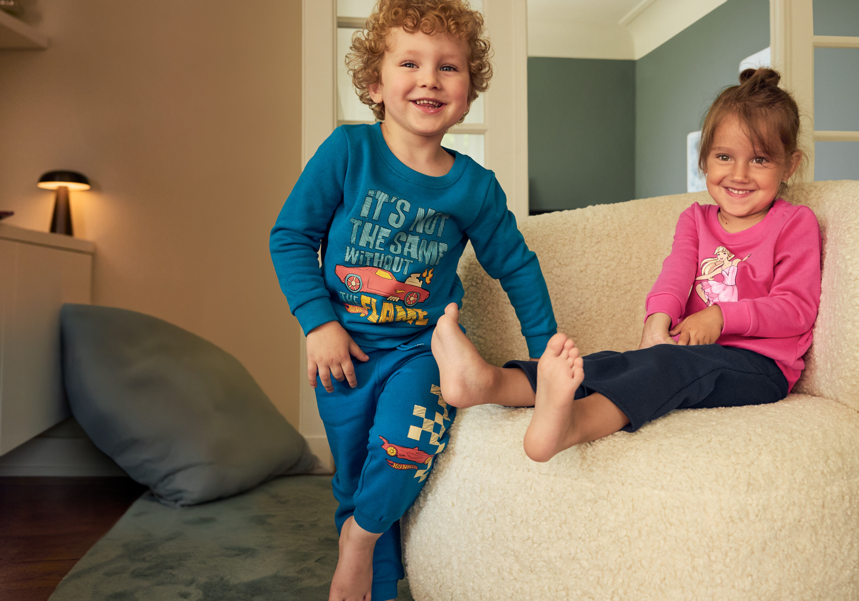 Egy fiú kék szettben és egy lány rózsaszín szettben ül egy bézs színű széken. A fiú 2 bolyhos belsejű, bőszárú termoleggingset visel.