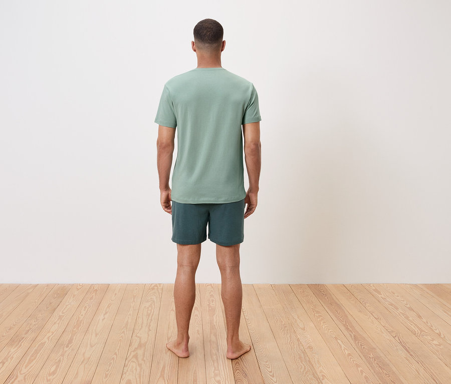 Egy férfi mezítláb áll háttal a nézőnek, zöld pólót és rövidnadrágot visel.