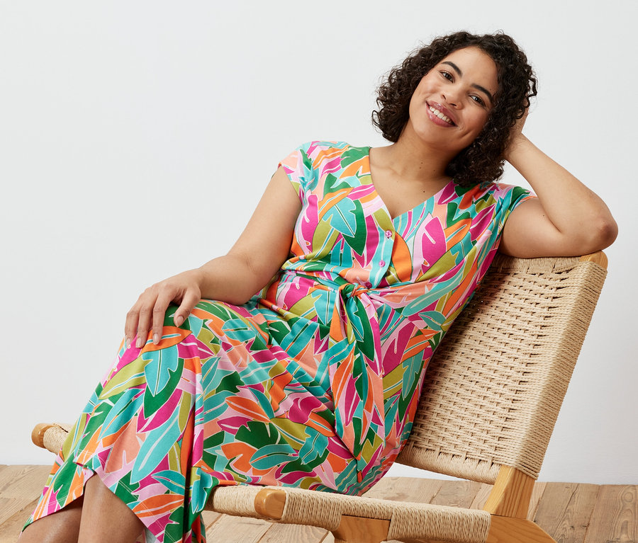 Nő ül egy széken és jersey ruhát visel csomókkal.