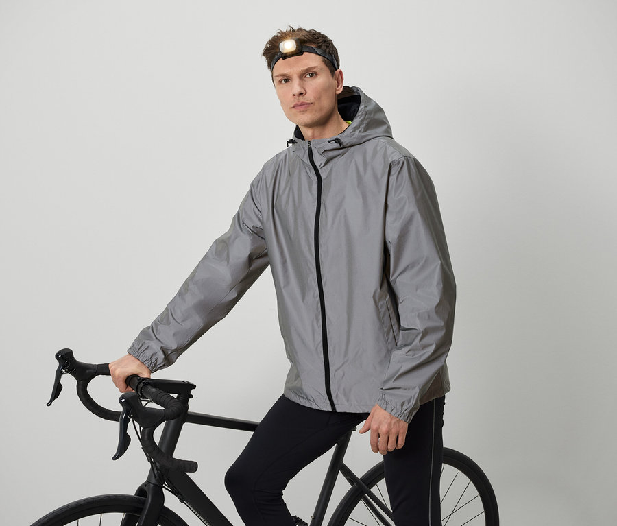 Férfi fejlámpával pózol egy kerékpárral, szürke kabátban.