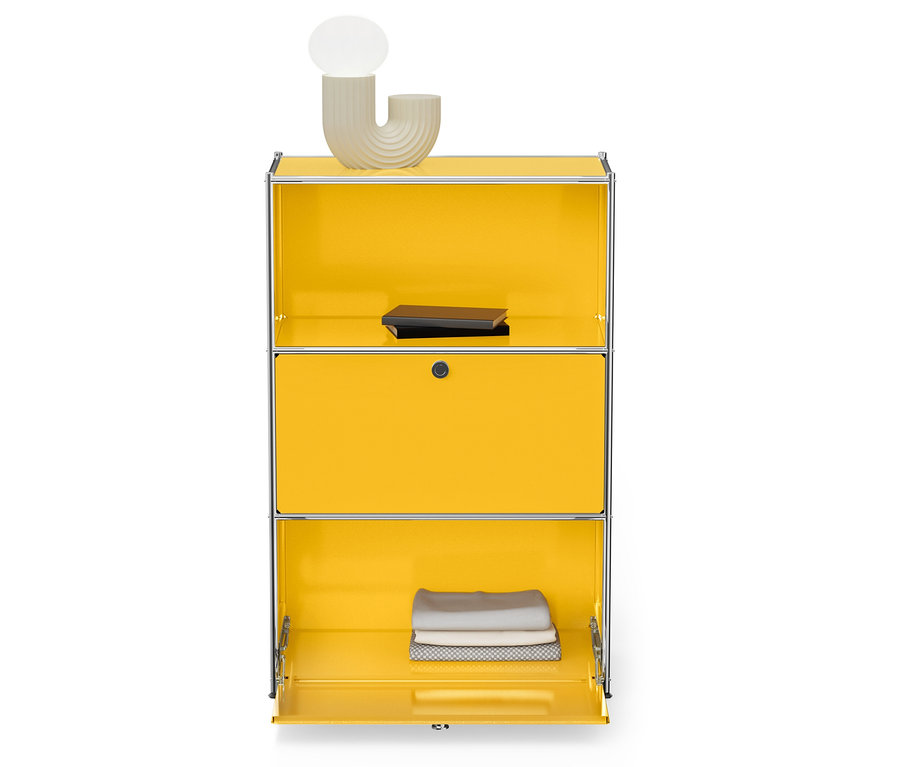 Sárga szekrény ezüst kerettel, tetején lámpa és könyv, alján összehajtott törölközők.