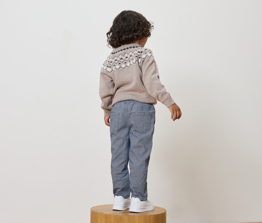 Hátulról látható fiú bézs mintás pulóvert, kék nadrágot és fehér cipőt visel.