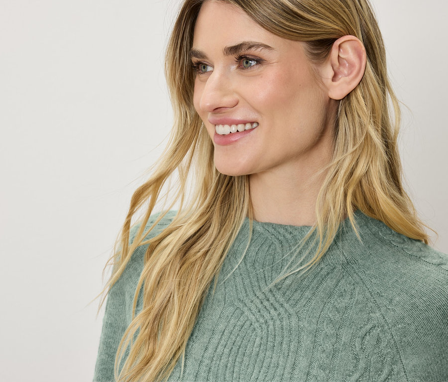 Egy mosolygó, szőke hajú nő profilja zöld pulóverben.