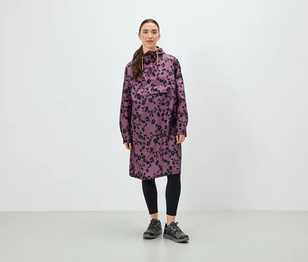 Egy nő áll, lila, fekete virágmintás tunikát, fekete leggingset és szürke cipőt visel.