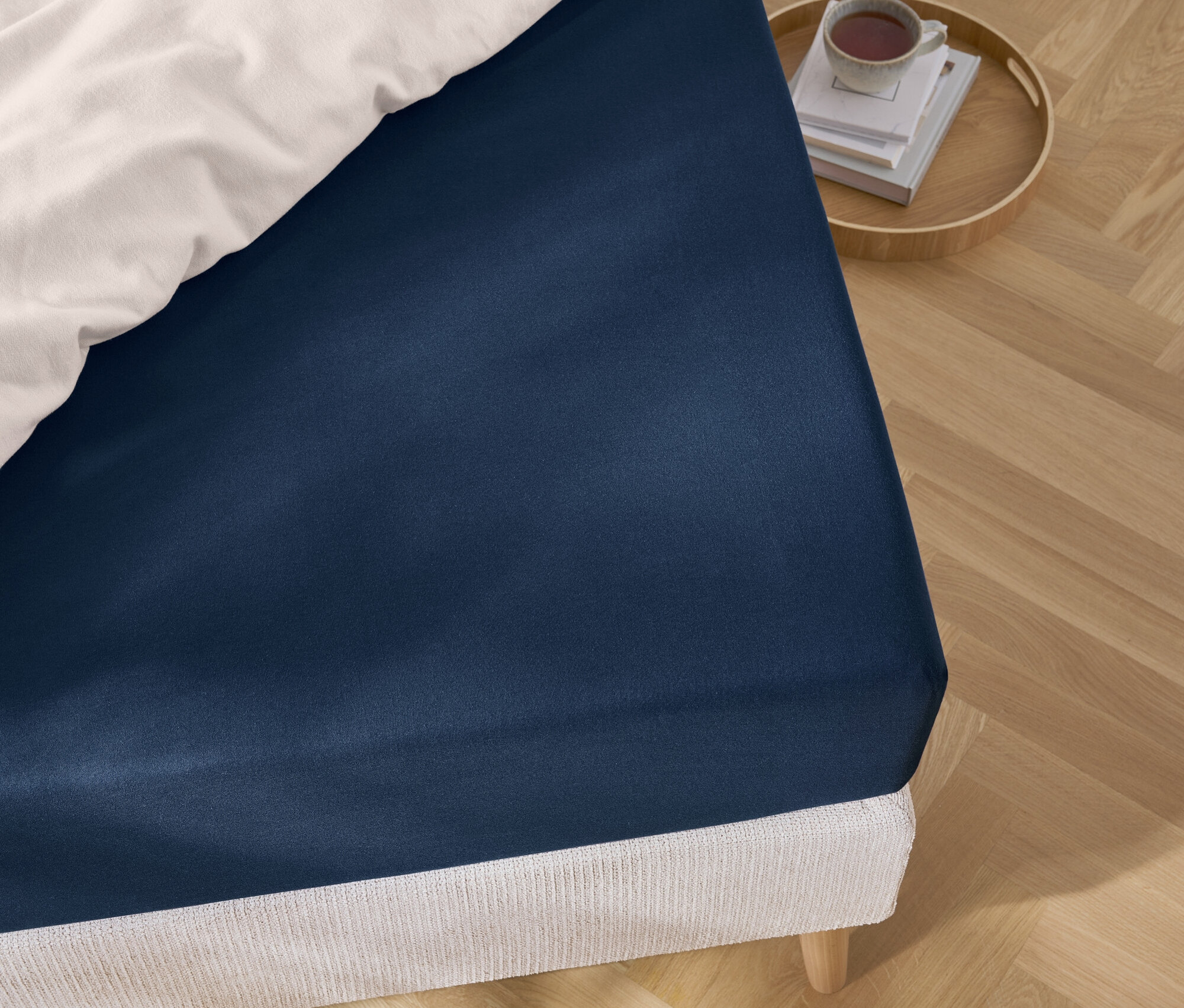 Egy kék lepedő részlete egy ágyon, fehér ágyneművel, valamint egy tálca könyvekkel és egy csészével.