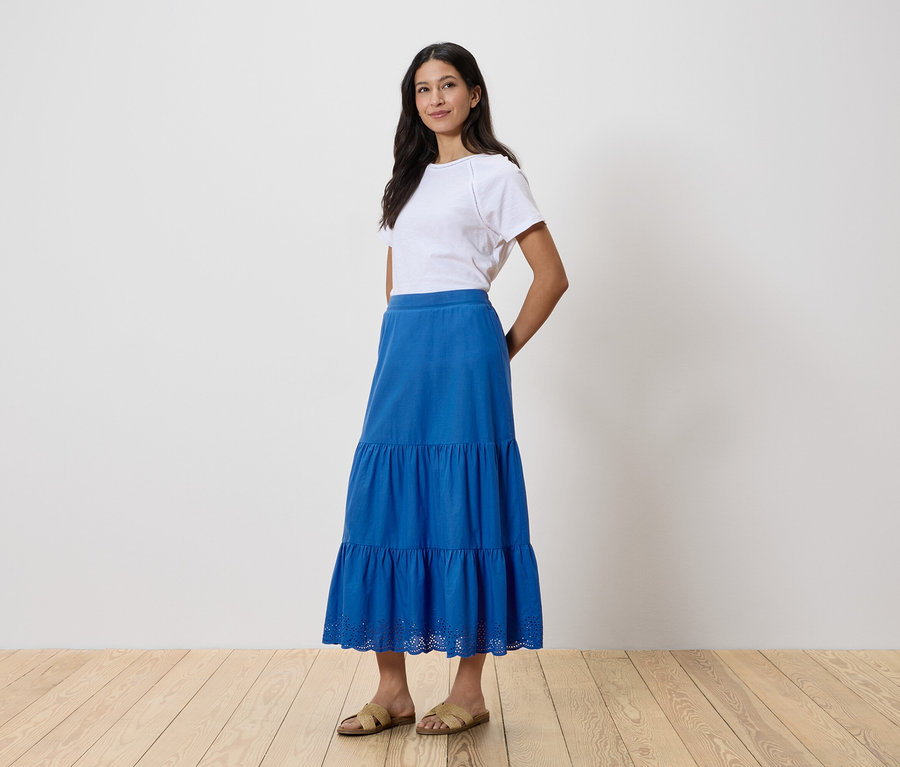 Nő áll, fehér pólót és kék szoknyát visel.