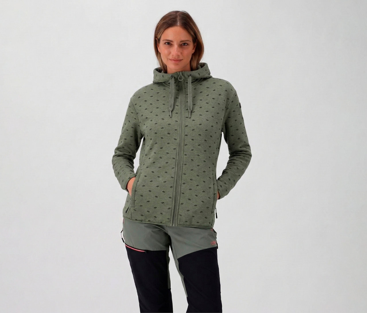 Kapucnis nő visel egy avokádó CMP női polárfelsőt kapucnival, és a kezét a zsebében tartja.