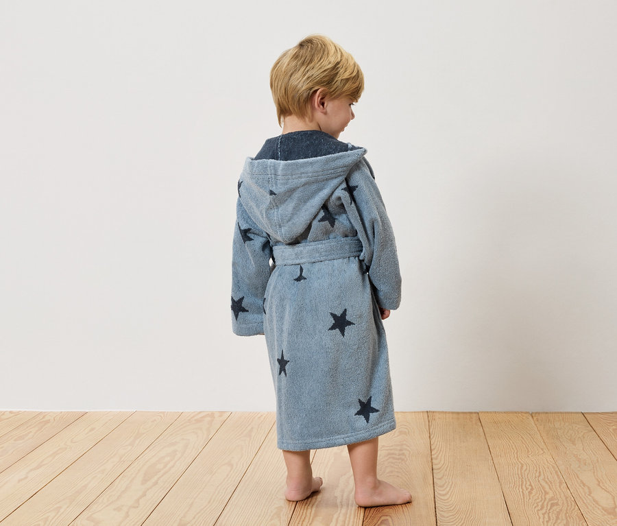 Egy gyermek áll háttal a kamerának, világoskék, csillagos köntösben.