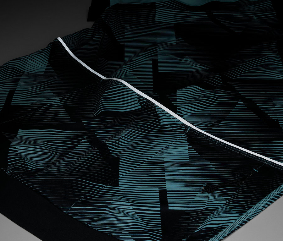 Egy ruhadarab közeli képe, fekete és türkiz színű, ismétlődő geometriai mintával, fehér csíkkal kiemelve.