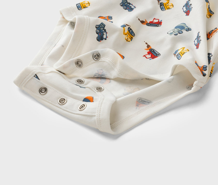 Közelkép egy fehér, építőipari járművekkel mintázott, patentos babaruháról.