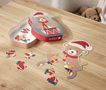 Egy Mikulás sapkás macis puzzle van szétszórva egy asztalon, mellette a doboza.