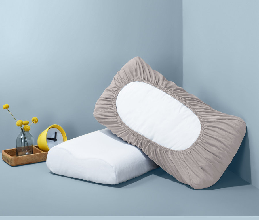 Két gumis párnahuzat, egy szürke és egy fehér, egymáson fekszenek a sarokban.