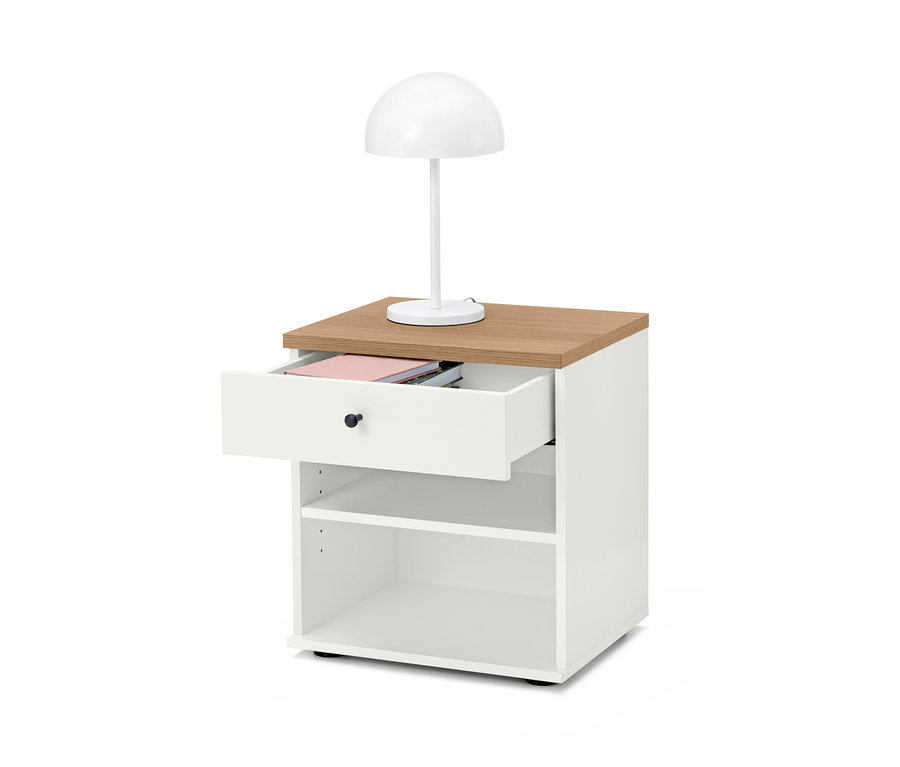 Fehér "Bekeson" éjjeliszekrény barna lappal és nyitott fiókkal. Az asztalon egy fehér lámpa áll.