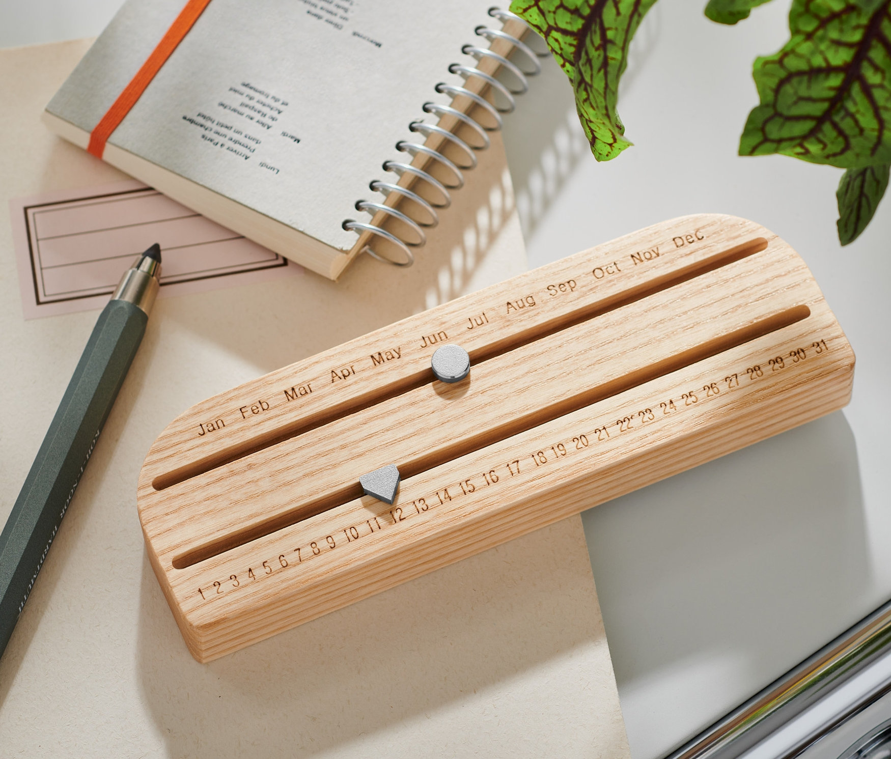 Egy fa öröknaptár egy asztalon fekszik egy jegyzettömb és egy toll mellett.