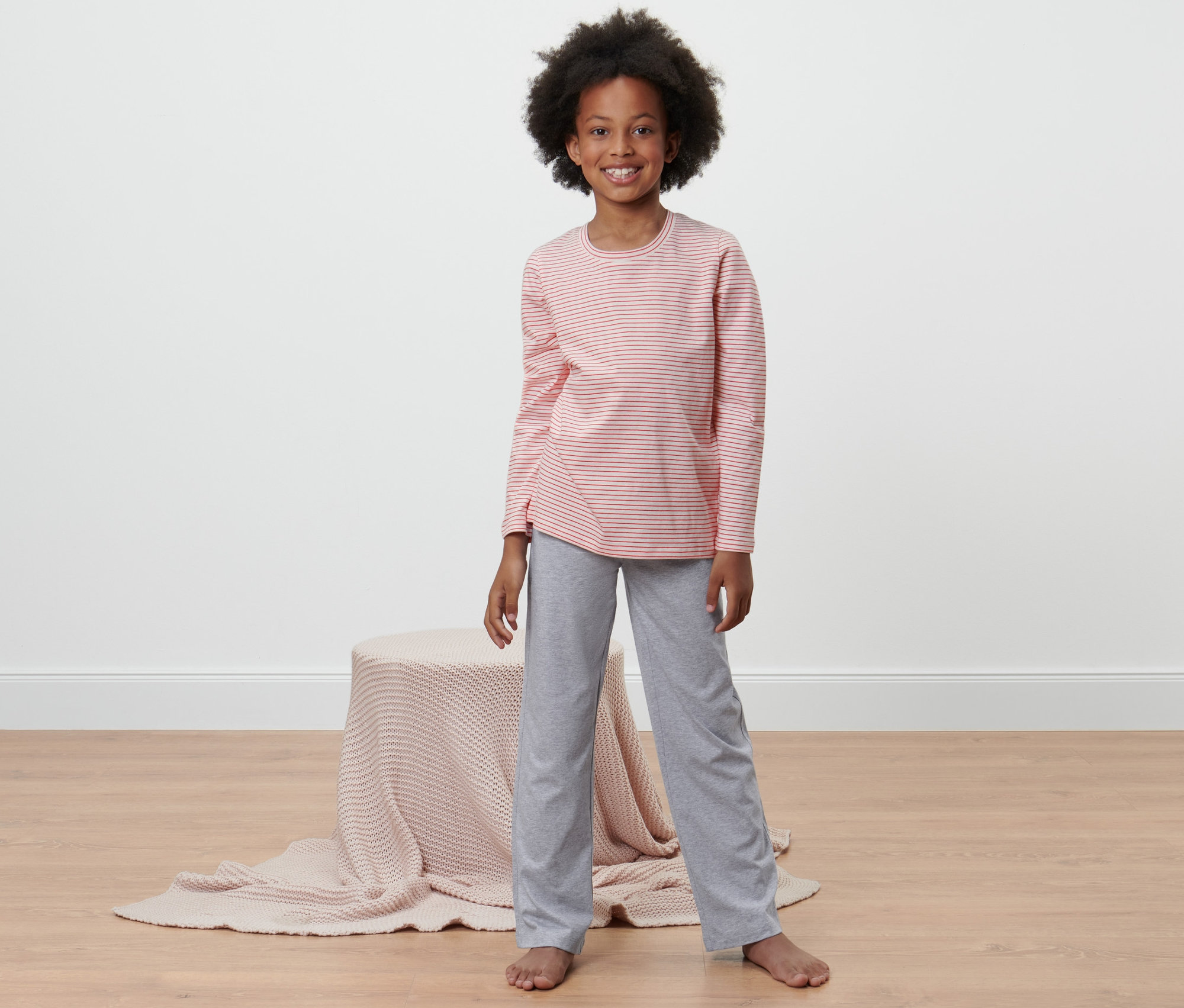 Egy lány szürke nadrágból és rózsaszín csíkos felsőből álló 2 részes lány pizsamát visel.