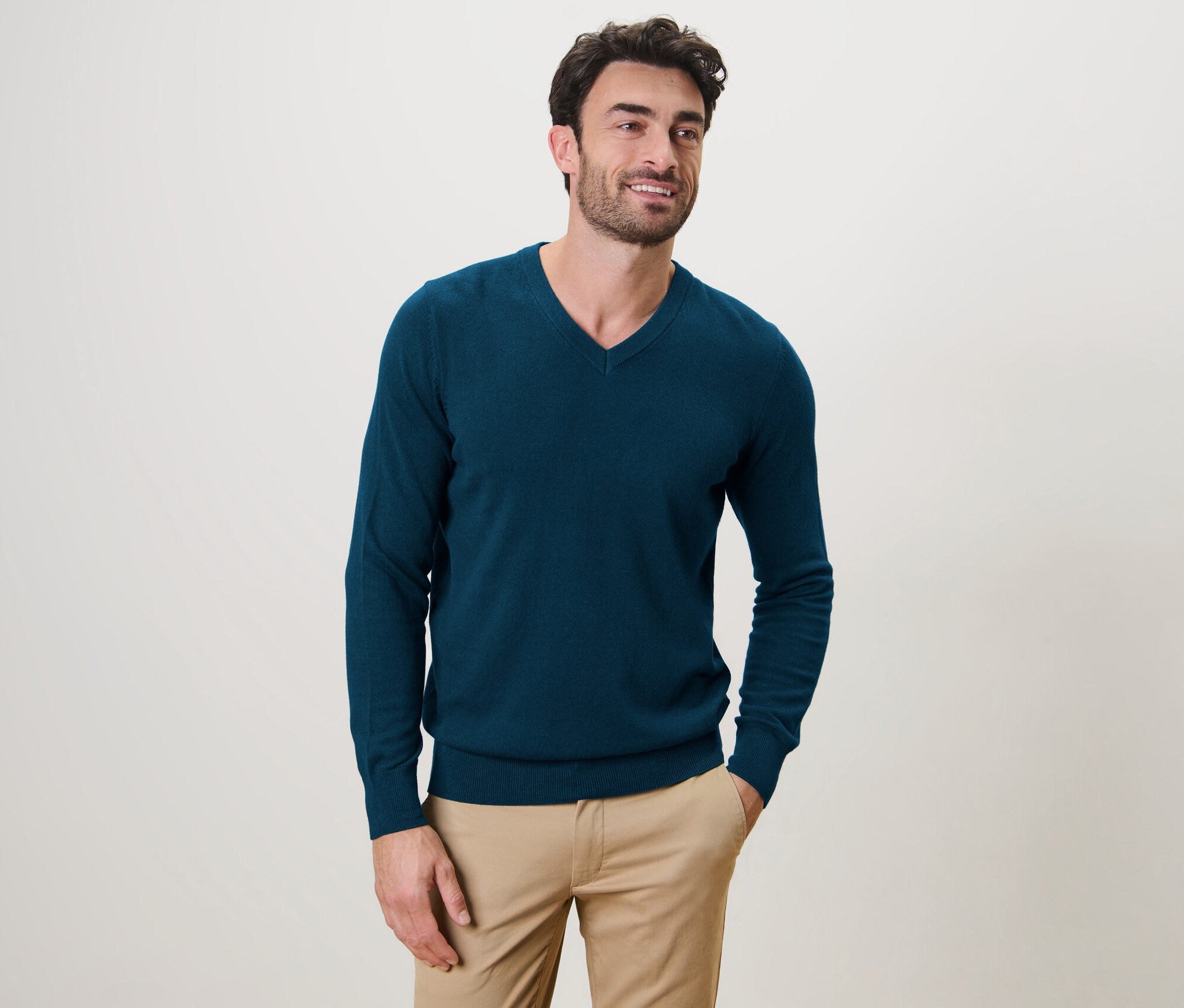 Férfi pózol, petrolkék V-nyakú pulóvert visel.