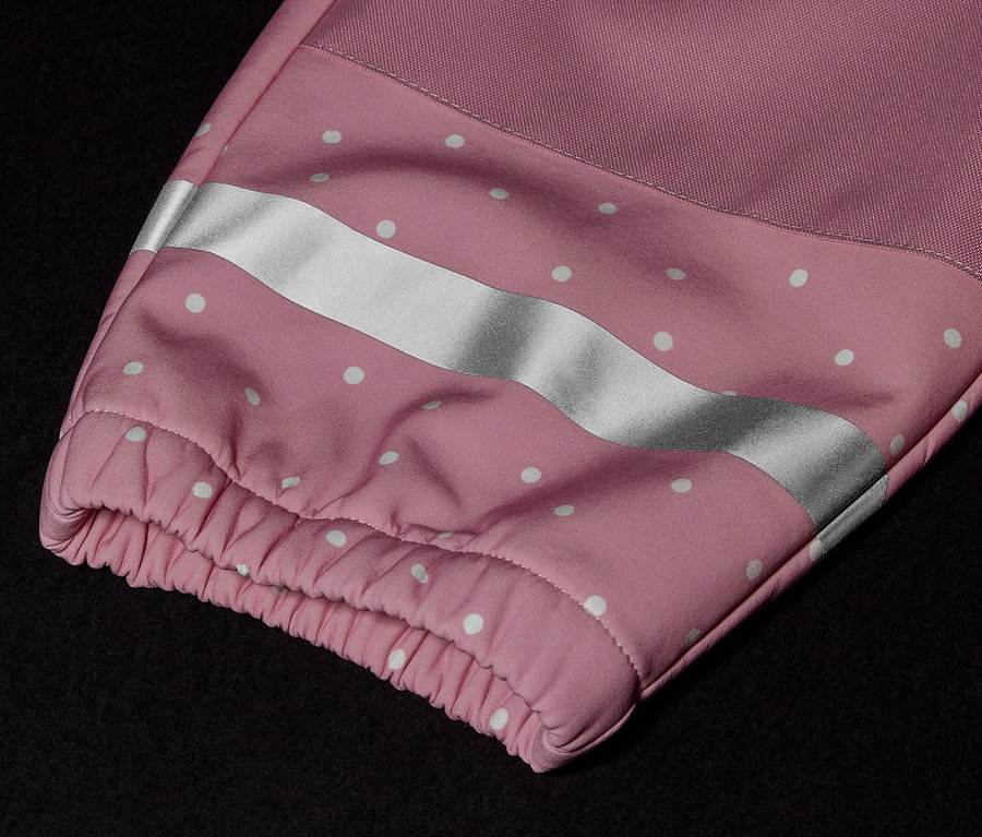 Egy gyermek softshell kezeslábas részlete rózsaszín ujjal, fehér pöttyökkel és fényvisszaverő csíkkal.