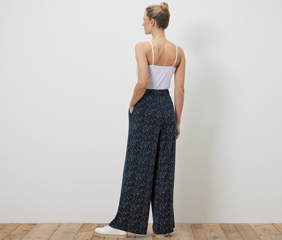 Egy nő háttal áll a kamerának, sötétkék-krémfehér, mintás palazzo nadrágot visel.
