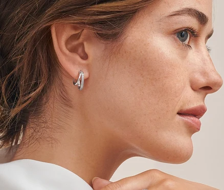 Profil egy barna hajú nő kontyban, aki dupla, beszúrós fülbevalót visel ródiummal bevont 925-ös ezüstből, cirkóniával, valamint egy női spirálgyűrűt ródiummal bevont 925-ös ezüstből, cirkóniával.