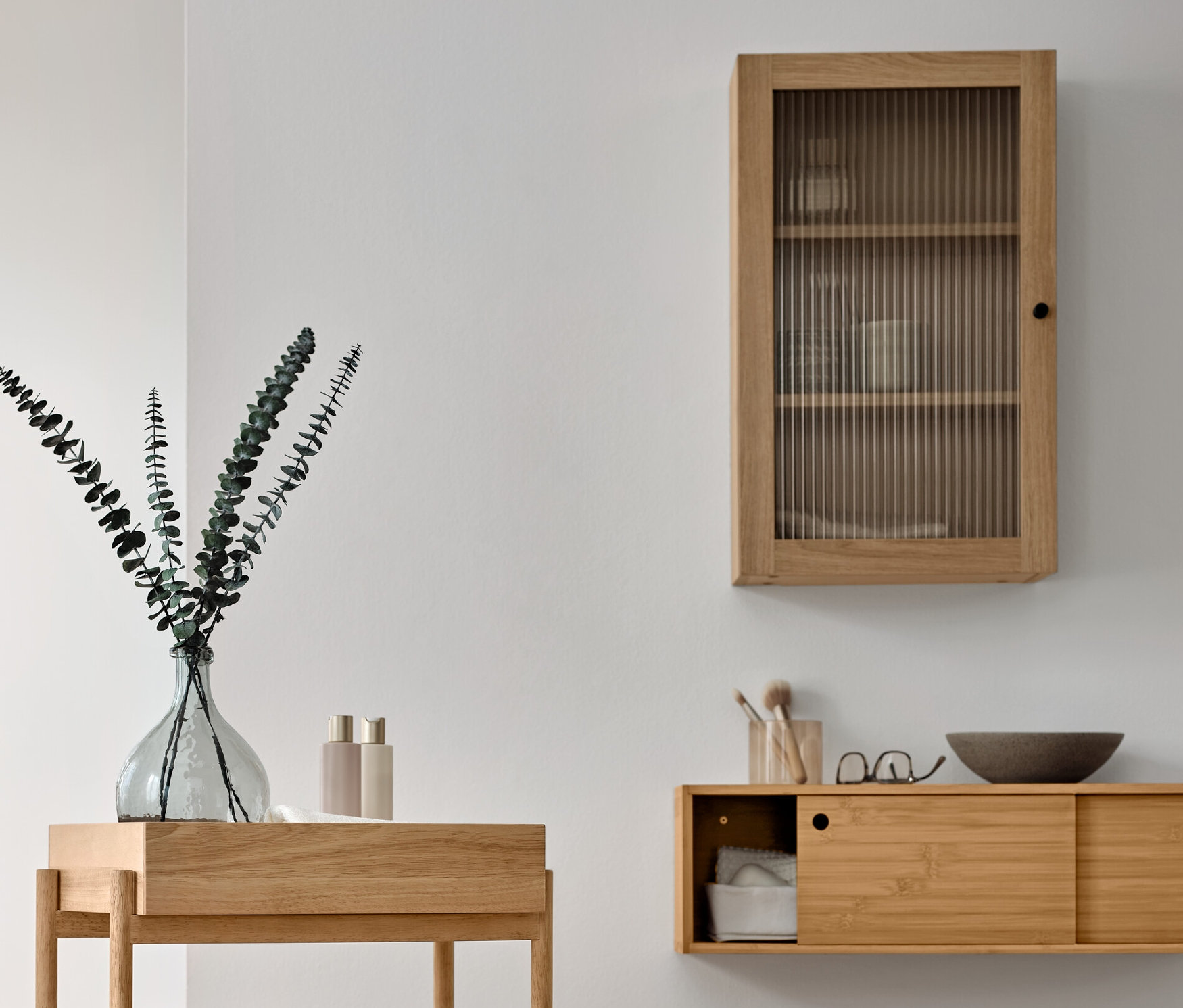 Egy fürdőszoba berendezése egy fa állópolccal, 3 rekesszel, egy faliszekrénnyel bordázott üvegajtóval és egy tömörfa törölközőtartó állvánnyal.