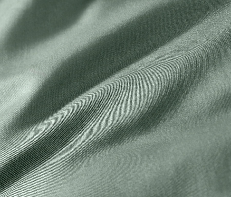 Közelkép egy zöld pamutszatén ágyneműről.