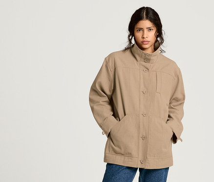 Nő pózol NAH/STUDIO újrahasznosított pamut parkában, mom farmerban és blúzban.