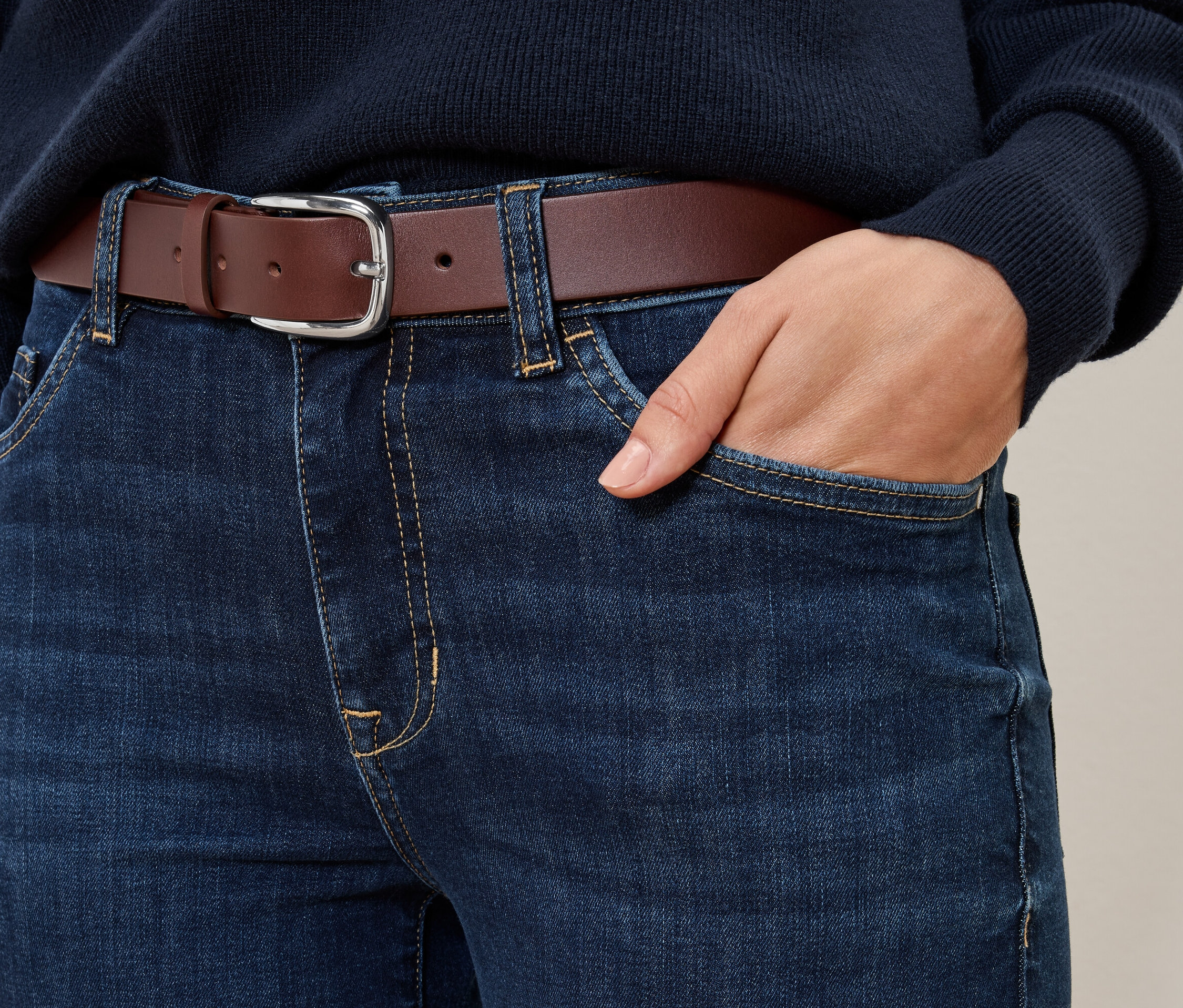 Egy farmer részlete egy konyak színű bőrövvel, egy kéz a zsebben.