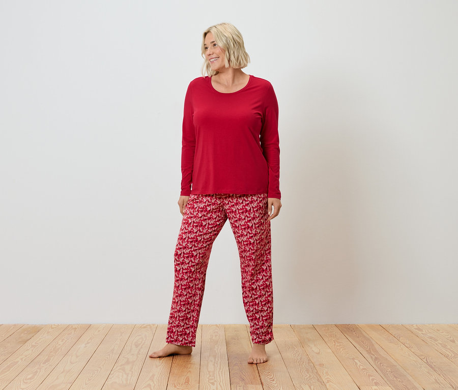 Egy szőke hajú nő áll egy fapadlón, és piros pizsamát visel.