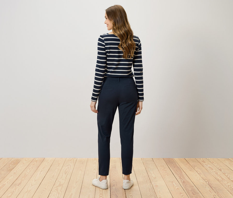 Hátulról látható egy barna hajú nő sötétkék nadrágban és csíkos pólóban.
