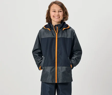 Mosolygó fiú Kinder softshell kabátban, kezével a zsebében.