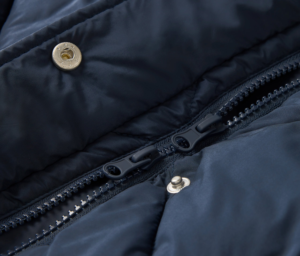 Egy sötétkék, steppelt dzseki részlete cipzárral és patentokkal.