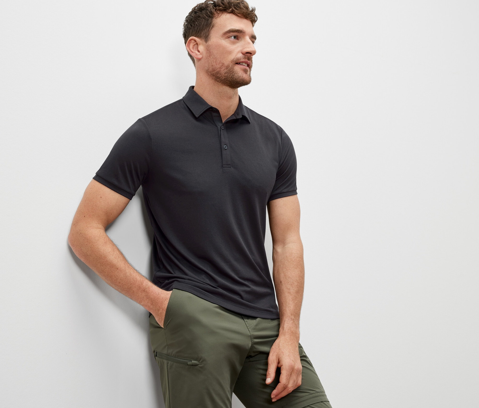 Férfi támaszkodik a falnak, antracit színű funkcionális pólóinget visel.